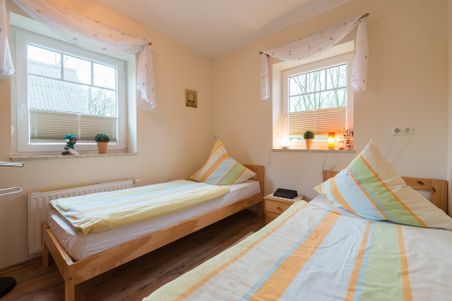 Helles Schlafzimmer mit zwei Einzelbetten, zwei Fenstern und schlichter Einrichtung.