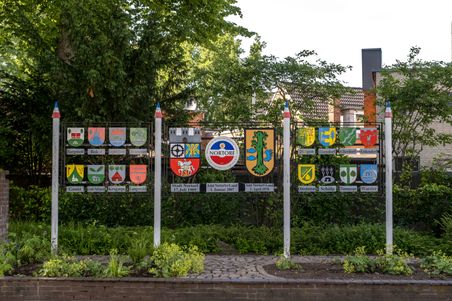 Schilder mit den Wappen der Gemeinden des Amts Nortorfer Land, umgeben von grüner Vegetation. Die Wappen sind auf einer Metallstruktur angebracht.