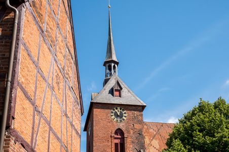 Die St. Marien Kirche in Rendsburg zeigt ihren markanten Kirchturm und das Fachwerk der Fassade unter einem klaren blauen Himmel.