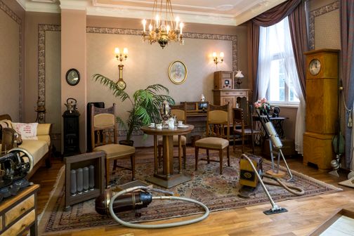 Ein historisch eingerichteter Raum im Elektromuseum Rendsburg zeigt antike Möbel und Elektrogeräte, darunter Staubsauger und ein Radio.