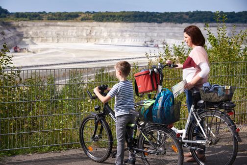Eine Frau und ein Junge mit Fahrrädern betrachten die kreidegruben in Lägerdorf. Sie stehen vor einem Zaun und scheinen eine Radtour zu machen.