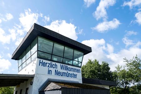 Der Kontrollturm des Flugplatzes Neumünster mit einem Schild 'Herzlich Willkommen in Neumünster' vor blauem Himmel und Wolken.