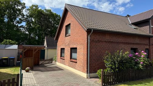 Außenansicht eines roten Backsteinhauses mit Satteldach, Einfahrt und Garten im Grünen.