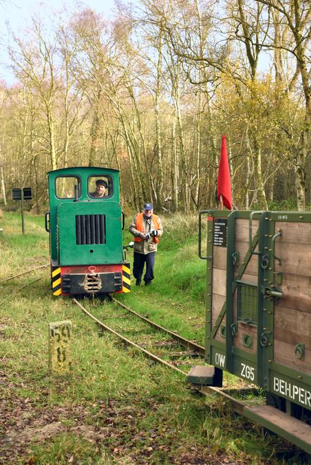Kurbahn in Holstein bei Bad Bramstedt mit grüner Lok, Güterwagen und Mann in Warnweste im Wald.