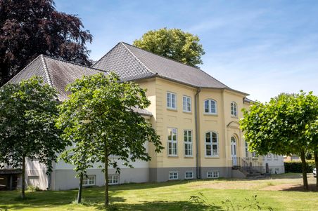 Das Casper-von-Saldern-Haus ist ein historisches Gebäude mit gelber Fassade und grauem Dach, umgeben von Bäumen und gepflegtem Rasen.