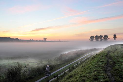 Eine Frau genießt auf ihrer Radtour entlang des Stördeiches den Sonnenaufgang.
