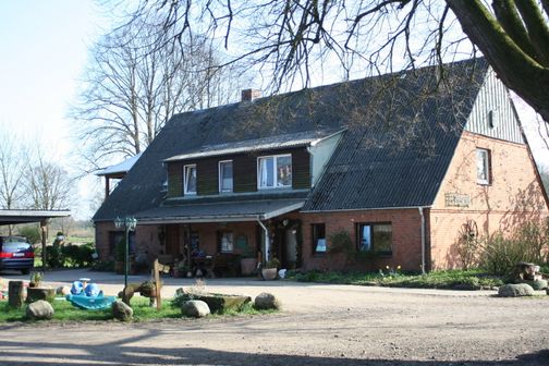 Das Landhaus 1878553_1720h zeigt eine rote Backsteinfassade, ein großes Steildach und einen Vorgarten mit Spielzeug und Steinen.