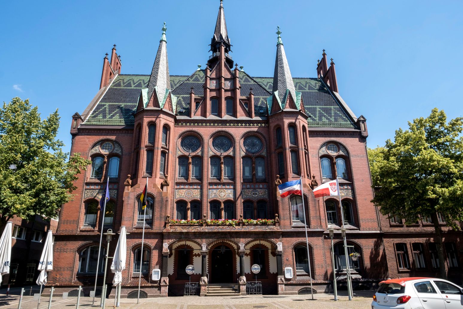 Das Alte Rathaus in Neumünster, ein beeindruckendes Gebäude aus roten Backsteinen mit Türmen und verzierten Fenstern, steht unter blauem Himmel.