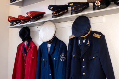 Uniformen und Mützen ausgestellt im Museumsstellwerk Rendsburg. Verschiedene historische Eisenbahnuniformen und -mützen sind an der Wand zu sehen.