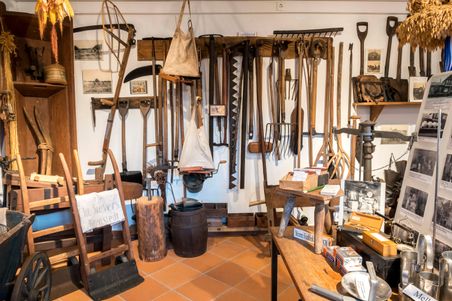 Ausstellung im Dorfmuseum Fockbek mit einer Sammlung alter landwirtschaftlicher Werkzeuge und Geräte an der Wand.
