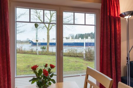 Wohnzimmer mit Blick auf ein großes Schiff auf dem Fluss, rote Vorhänge und Stehlampe im Raum.