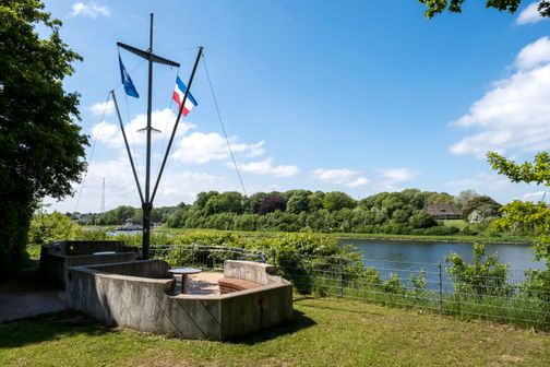 Aussichtspunkt in Schacht-Audorf mit Fahnenmast und Sitzbereich, umgeben von grüner Landschaft und Blick auf einen Fluss.