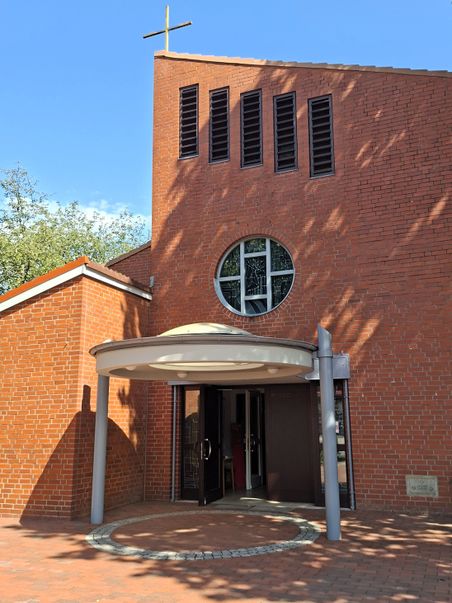 Eingang der Jesus Guter Hirt-Kirche in Bad Bramstedt. Die Kirche hat eine Fassade aus rotem Backstein und ein Kreuz auf dem Dach.