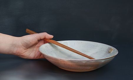 Eine Hand hält eine Keramikschale mit einem Holzstab. Der Hintergrund ist dunkel und schlicht.