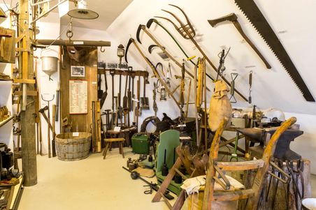 Ein Raum mit einer Sammlung alter landwirtschaftlicher Werkzeuge und Geräte, die an den Wänden hängen und auf dem Boden stehen.