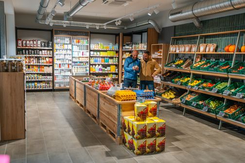 Umgeben von Regalen mit Naturkosmetik und frischem Obst und Gemüse.