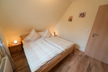 Gemütliches Schlafzimmer mit Doppelbett, Nachttischen und warmem Licht; zwei kleine Bilder an der Wand.