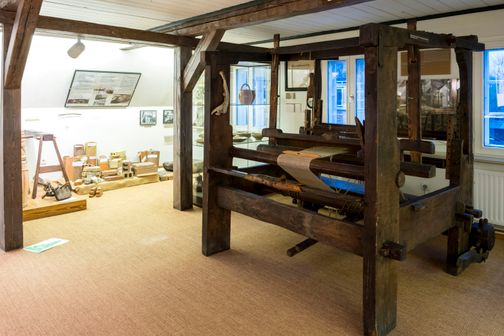 Ein alter Webstuhl und historische Werkzeuge in einem Raum des Heimatmuseums Hohenwestedt. Die Ausstellung zeigt traditionelle Handwerkskunst.