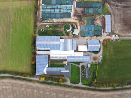 Luftaufnahme vom Hof Neuhörn mit mehreren Gebäuden, die Solarpaneele auf den Dächern haben. Umgeben von Feldern und Grünflächen.