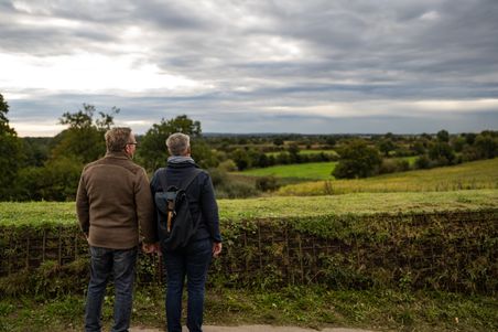 Ein Paar hält sich an den Händen und genießt die Aussicht auf die grüne Landschaft unter einem bewölkten Himmel.