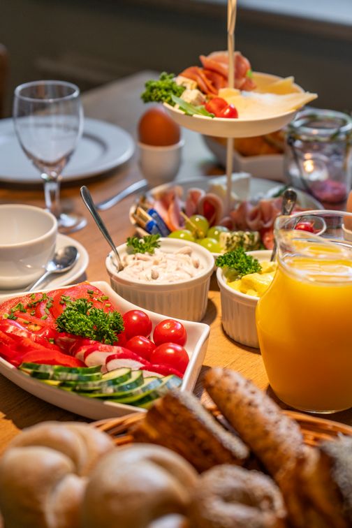 Ein einladender Frühstückstisch mit Brötchen, Aufschnitt, frischem Gemüse, Saft und verschiedenen Dips.