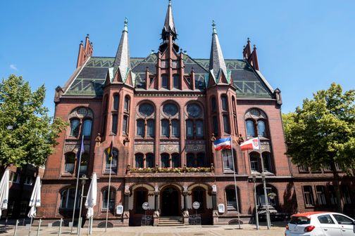 Das Alte Rathaus in Neumünster, ein beeindruckendes Gebäude aus roten Backsteinen mit Türmen und verzierten Fenstern, steht unter blauem Himmel.