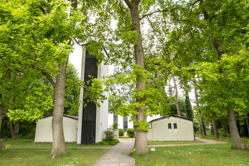 Die Kreuzkirche Schülp ist von üppigem Grün umgeben. Der weiße Bau mit schwarzem Turm fügt sich harmonisch in die Natur ein.
