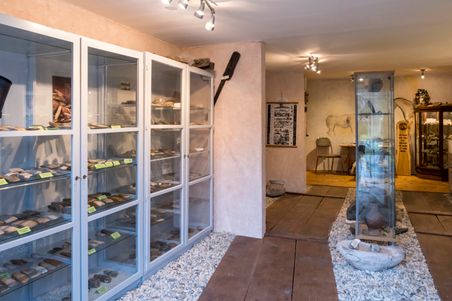 Ein Museumsraum mit Vitrinen, die archäologische Artefakte zeigen. Der Boden ist mit Kieselsteinen bedeckt, und an den Wänden hängen Bilder.