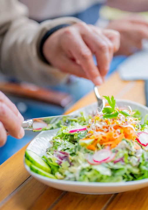 Ein Teller mit frischem Salat, garniert mit Karotten, Radieschen und Petersilie. Hände bereiten den Salat mit Besteck zu.