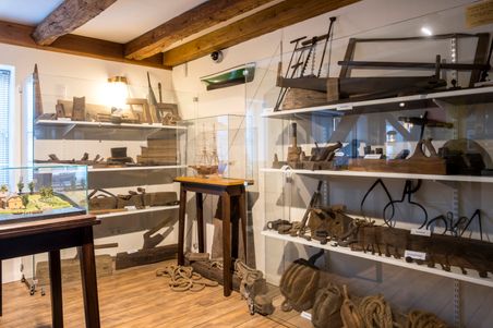 Ein Raum im Schifffahrtsarchiv Rendsburg zeigt historische maritime Werkzeuge und Schiffsmodelle in Vitrinen. Holzbalken und Holzboden ergänzen das Ambiente.