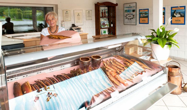 Bei Reese steht eine Fischtheke mit geräuchertem Fisch; dahinter eine Verkäuferin im Verkaufsraum.