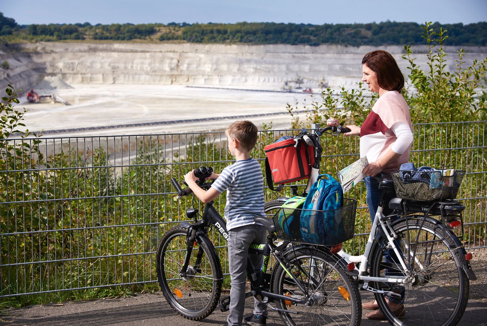 Mutter und Sohn mit Fahrrädern blicken auf eine Kreidegrube mit Bagger in Lägerdorf, Kreis Steinburg