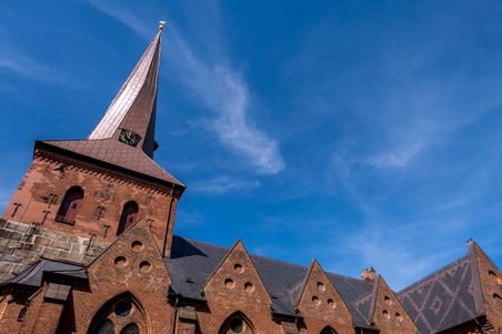 Die Sankt Martin Kirche in Nortorf zeigt ihre beeindruckende Architektur mit rotem Backstein und einem hohen, spitzen Turm unter einem klaren blauen Himmel.