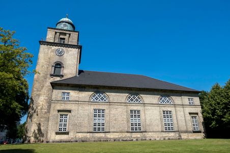 Die Vicelinkirche in Neumünster, ein historisches Gebäude mit einem hohen Turm und großen Fenstern, steht vor einem strahlend blauen Himmel.