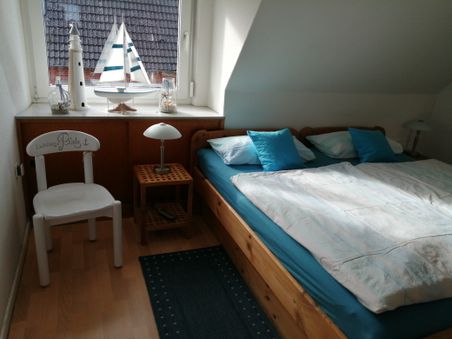 Kleines Schlafzimmer mit Holzbett, blau-weißer Bettwäsche und maritimer Deko auf der Fensterbank.