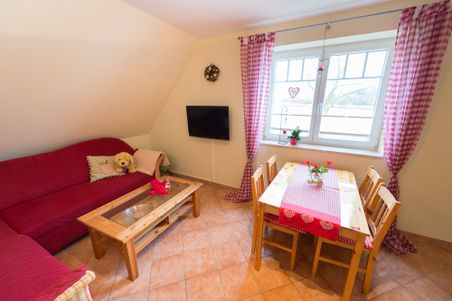 Gemütliches Wohnzimmer mit rotem Sofa, Holztisch, Esstisch am Fenster und Wandfernseher. Der Titel 20150327-8RU_8935 ist nicht aussagekräftig.