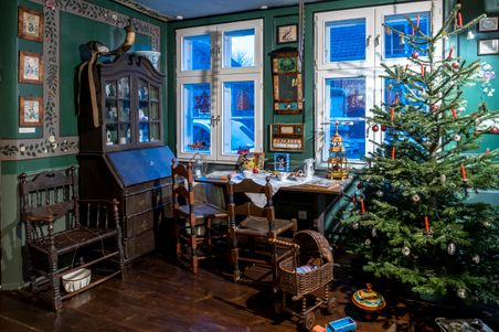 Ein traditionell eingerichtetes Zimmer im Heimatmuseum Hohenwestedt mit antiken Möbeln, einem geschmückten Weihnachtsbaum und nostalgischen Dekorationen.