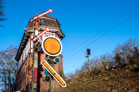 Ein historisches Stellwerk mit Signalanlage vor blauem Himmel. Das Gebäude ist aus Backstein und Fachwerk, umgeben von kahlen Bäumen.