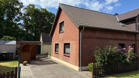 Außenansicht eines roten Backsteinhauses mit Satteldach, Einfahrt und Garten im Grünen.