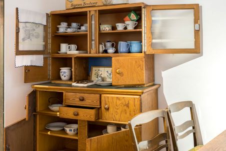 Ein rustikaler Küchenschrank mit offenem Geschirr, Tassen und einem Bonbonkarton im Dorfmuseum Fockbek.