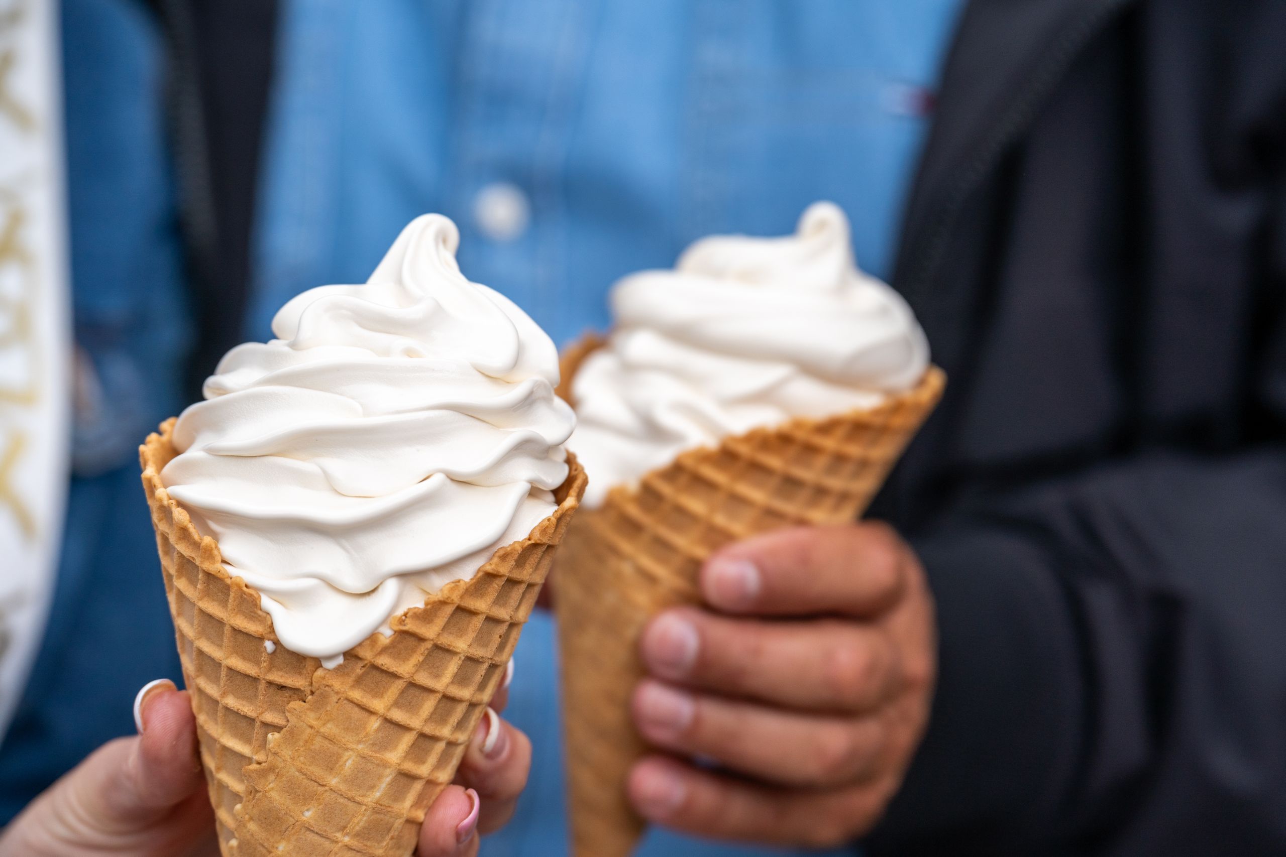 Zwei Personen halten große Waffelhörnchen mit cremigem Eis. Die Szene vermittelt sommerlichen Genuss.