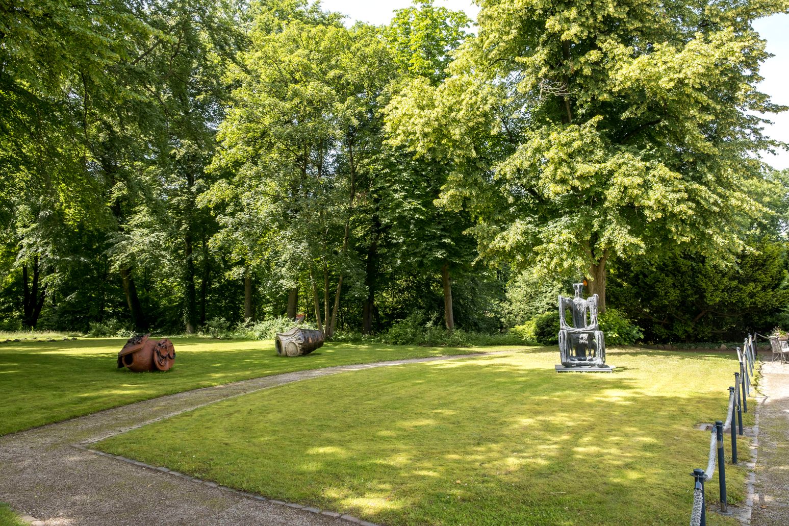 Skulpturen im Gerisch-Skulpturenpark Neumünster, umgeben von grünen Bäumen und gepflegtem Rasen. Ein Weg führt durch den Park.