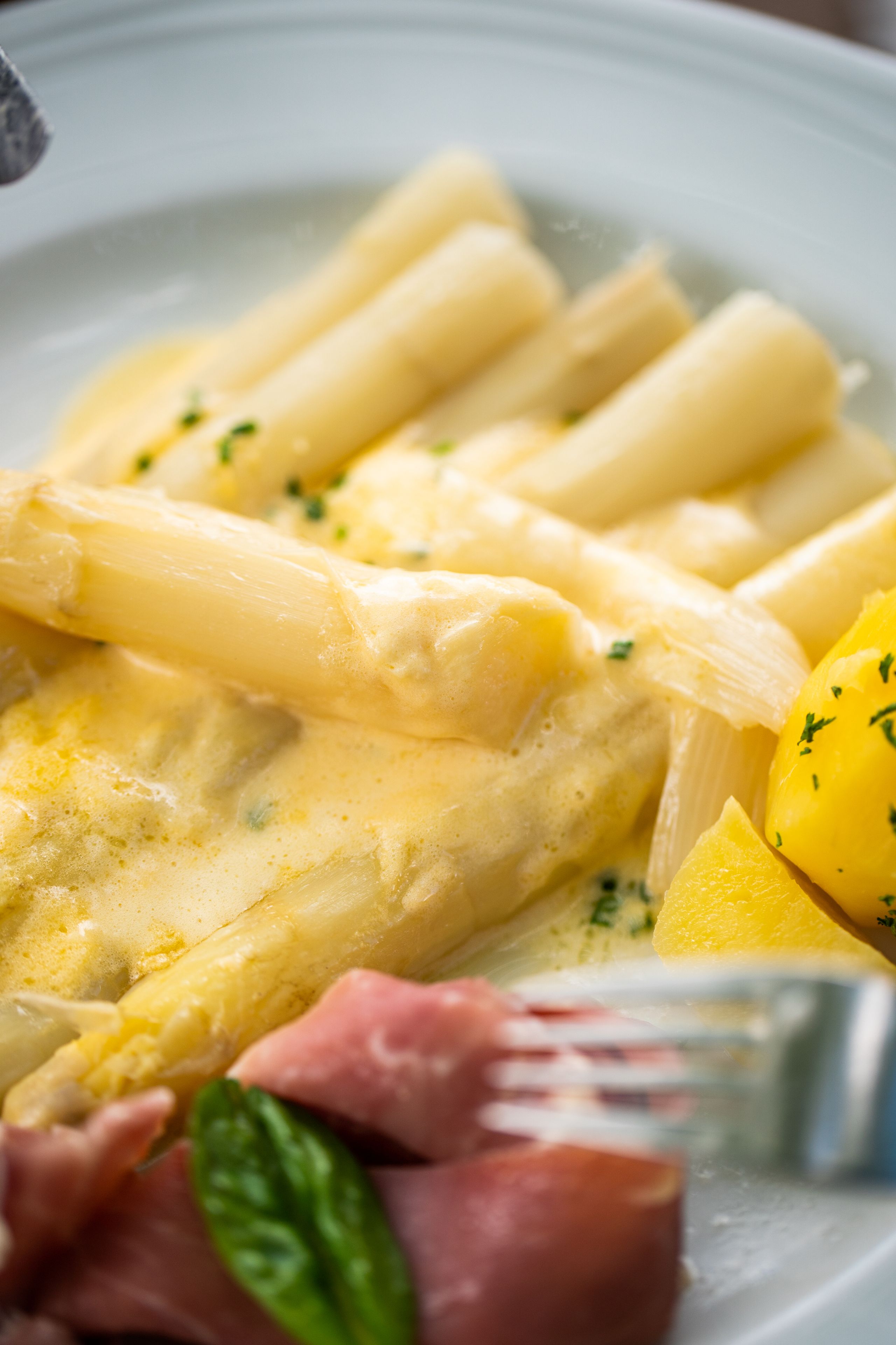 Spargel mit Sauce Hollandaise, Kartoffeln und Schinken auf einem Teller. Ein klassisches Gericht, das Frische und Genuss vereint.