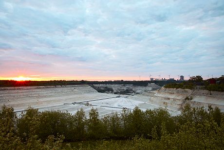 Die weitläufigen Kreidegruben Lägerdorf bei Sonnenuntergang, umgeben von Bäumen. Am Horizont sind Windkraftanlagen zu sehen.