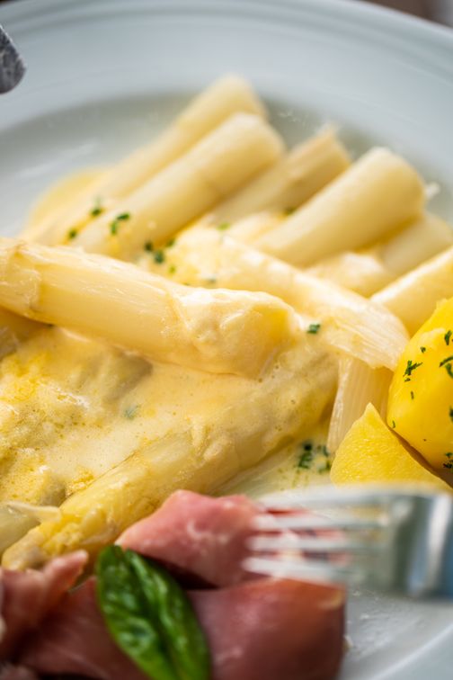 Spargel mit Sauce Hollandaise, Kartoffeln und Schinken auf einem Teller. Ein klassisches Gericht, das Frische und Genuss vereint.