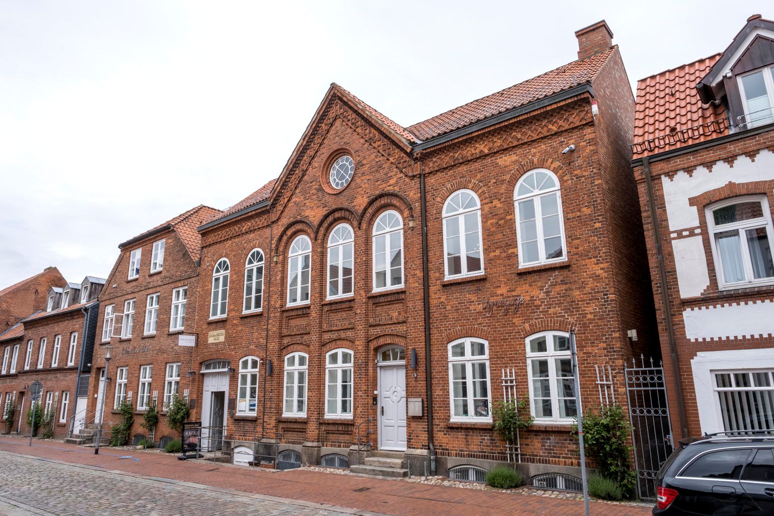 Ein historisches Backsteingebäude mit weißen Fenstern und einem Schild, das auf ein Museum hinweist. Es befindet sich in einer gepflasterten Straße.