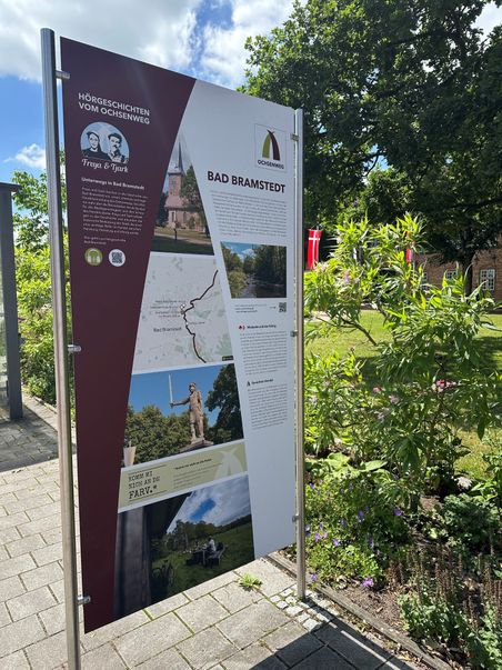 Eine Infotafel in Bad Bramstedt informiert über den Ochsenweg. Es zeigt Bilder und Texte zur Geschichte und Sehenswürdigkeiten der Region.