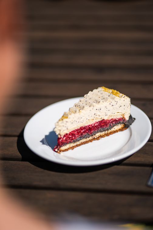 Ein Stück Kuchen mit Mohn, Himbeeren und Sahne auf einem weißen Teller.