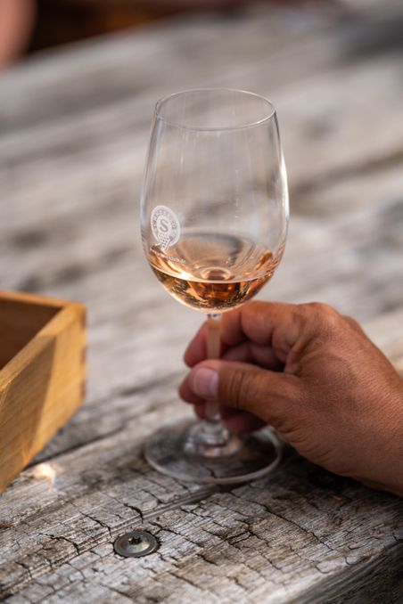Ein Glas Roséwein wird von einer Hand auf einem rustikalen Holztisch gehalten. Das Glas trägt das Logo von Schneekloth.