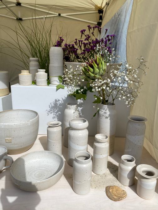 Keramikausstellung mit grauen Vasen und Schalen, umgeben von Blumen und Pflanzen in einem Zelt.